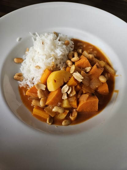 Eine Portion angerichtet auf einem weißen Teller. Als Beilage wird Reis serviert, garniert wird mit zerstoßenen Erdnüssen.