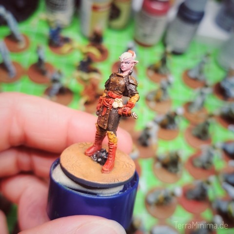 Eine Hand hält eine weibliche gelesene Figur in Händen, die seitlich mit genervtem Blick guckt. Im Hintergrund mehrere unscharfe Miniaturen.