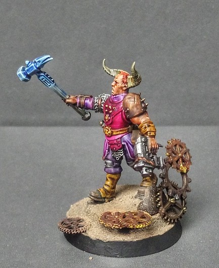 Photo of an Age of Sigmar Miniature painted and finished. He looks rather normal, except that he has horns, is wielding a Bolter and there is a lot of clock work stuff around him. 