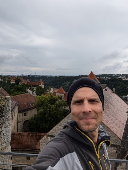 Selfie eines alten Mannes in Sportklamotten auf dem höchsten frei zugänglichen Punkt der Burg zu Burghausen. Im Hintergrund sieht man den beinahe kompletten Verlauf der angeblich längsten Burg der Welt