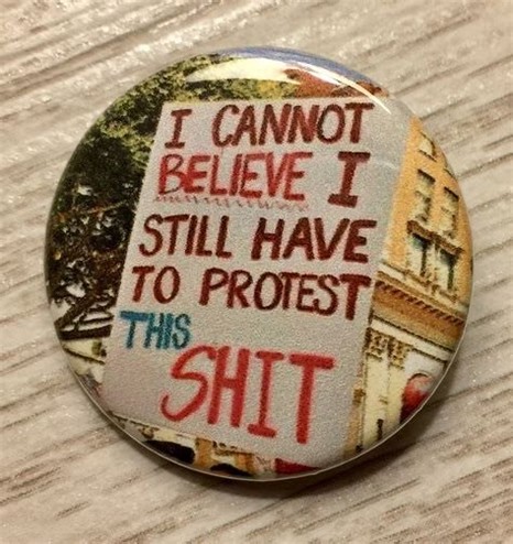 A picture of a button showing a protest sign that reads „I cannot believe I still have to protest this shit“. 