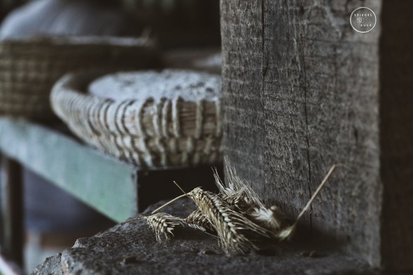 Drapierte Getreideähren. Im Hintergrund ungebackenes Brot in Körben.