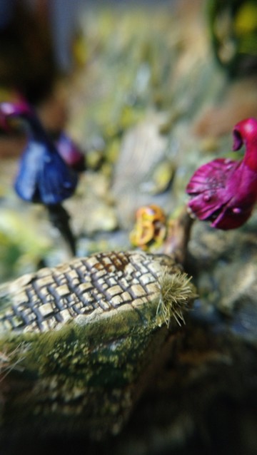 Close-up photo of a ruined piece of masonry with some grass and giant colourful blue and violet mushrooms.